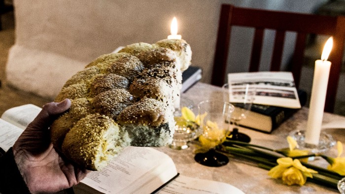 En person holder en stor kage på et bord med lysstake, blomster og bøger