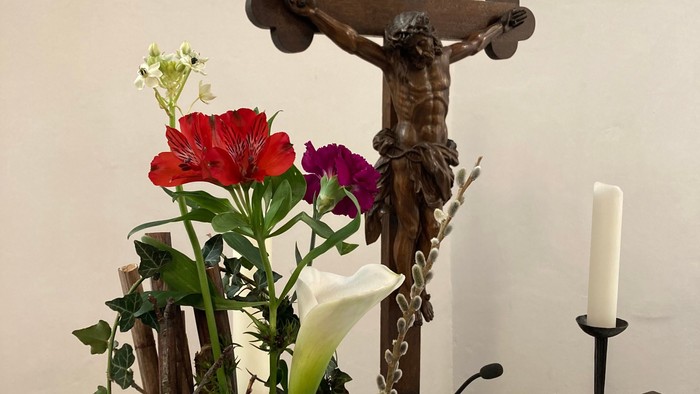 Ein Kreuz mit Jesusfigur, ein Blumenstrauß und eine aufgeschlagene Bibel