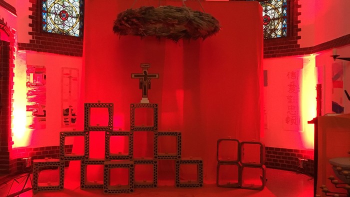 Die Kirche ist in rotes Licht getaucht, mit einem großen Kreuz und bunten Glasfenstern.