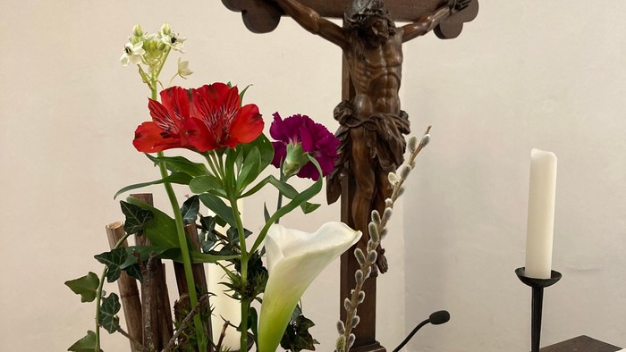 Ein Kreuz mit Jesusfigur, ein Blumenstrauß und eine aufgeschlagene Bibel