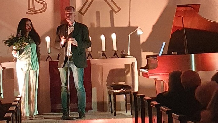 Musiker, die auf einer Bühne in einer Kirche mit dekorativen Kreuzsymbolen an der Wand auftreten.