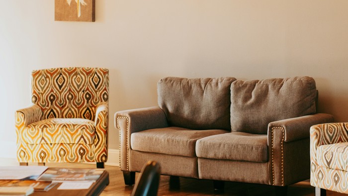 Gemütliches Wohnzimmer mit beigefarbenem Sofa und zwei gemusterten Sesseln vor beigefarbenen Wänden und Dekorationen