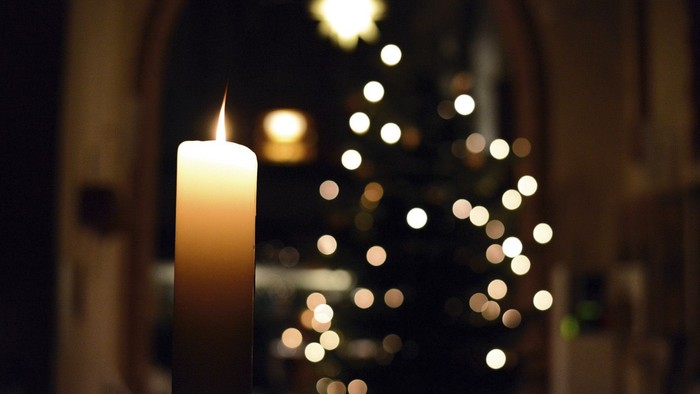 Eine brennende Kerze vor einem beleuchteten Weihnachtsbaum in einer Kirche.