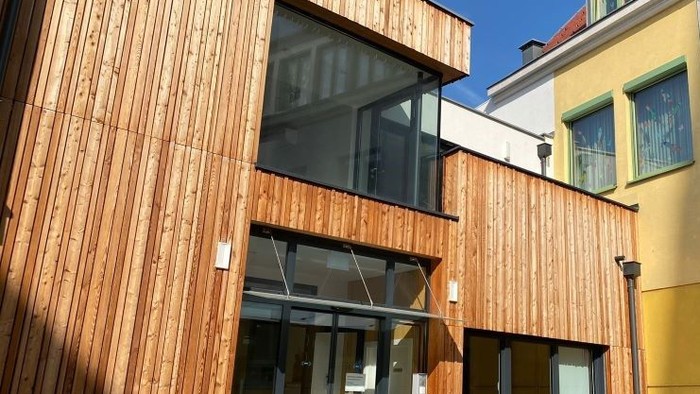 Moderne Holzfassade eines Gebäudes mit großen Fenstern und einem Balkon.