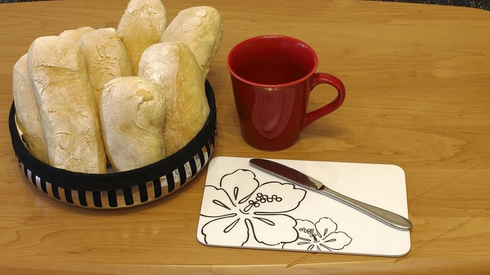 En korb med brød, en rød tæppe og en kniv på bordet