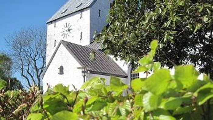 Et hvidt kirkebygning med klokketårn og grønne planter i forgrunden