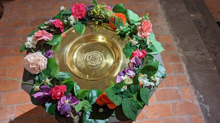 Eine goldene Schale, umgeben von bunten Blumen auf einem Ziegelboden.