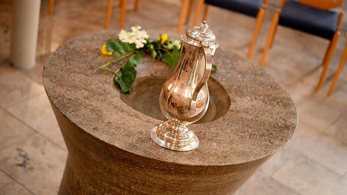 Ein silberner Kerzenhalter auf einem steinernen Tisch mit Blumen.