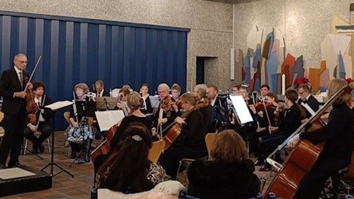 Et orkester opfører en koncert med et publikum, der opmærksomt følger med, og en dirigent, der leder musikerne.