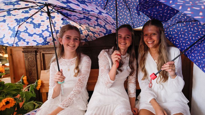 Tre pige i hvide kjoler holder blå paraplyer.