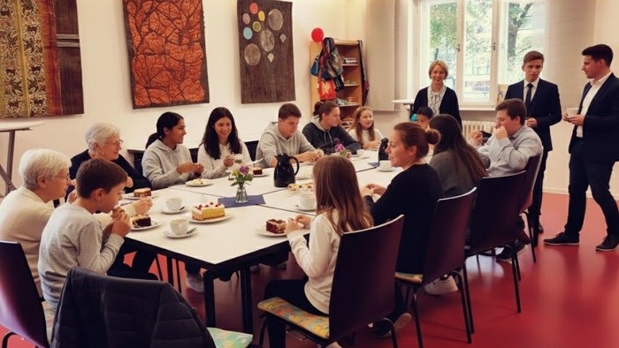 Eine vielfältige Gruppe genießt ein geselliges Beisammensein mit Tee und Gebäck an einem langen Tisch.