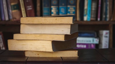 En stak gamle bøger på en hylde omgivet af forskellige farverige bøger og mapper.