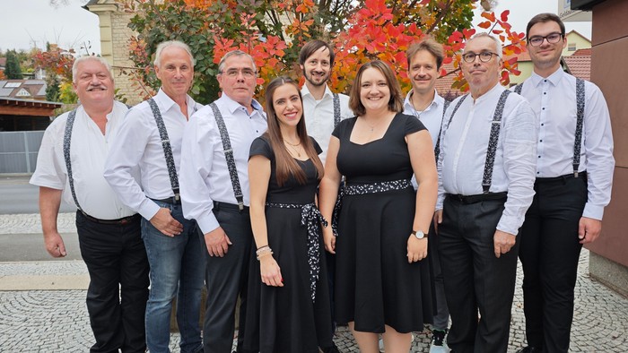 Gruppe von acht Personen, die sich im Freien in Herbstkleidung gemeinsam fotografieren lassen, mit buntem Laub im Hintergrund.