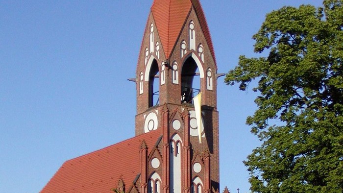 Die Kirche hat einen hohen Turm mit spitzem Dach und Zifferblatt.