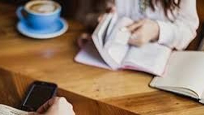 En kvinde sitter ved et bord og ser på sit mobiltelefon, mens der er en blå tektabel og en laptop på bordet.