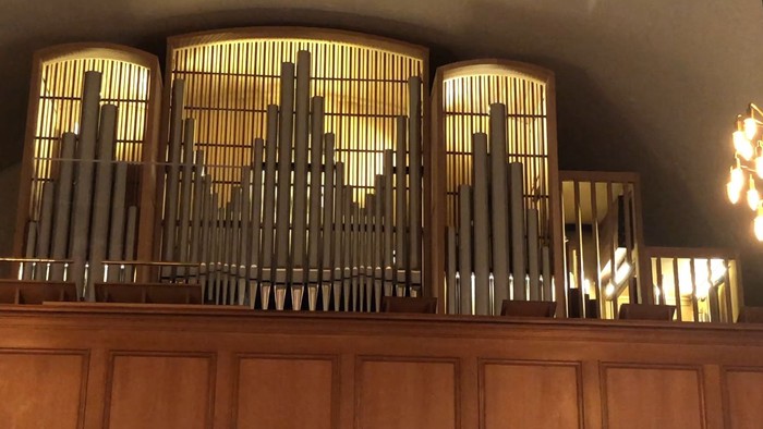 Et nærbillede af et stort pibeorgel med oplyste piber og træbeklædning, badet i varmt lys.