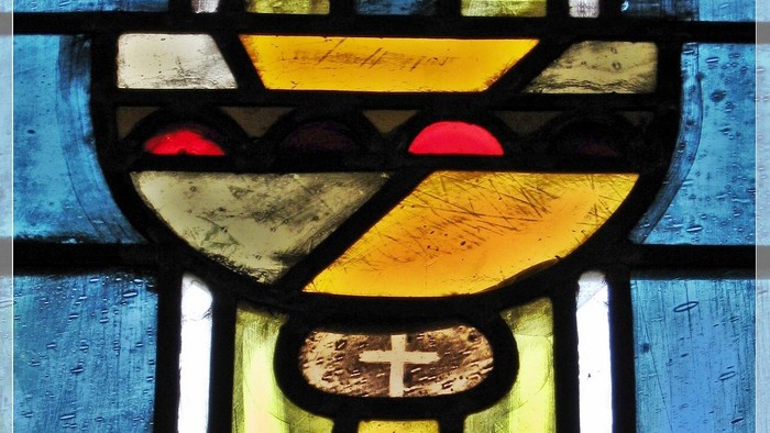 Buntglasfenster mit der Darstellung eines Kelchs mit Kreuz auf blauem Hintergrund.