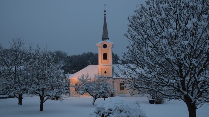 Schneebedeckte Kirche mit hohem Turm und kahlen Bäumen im Winter