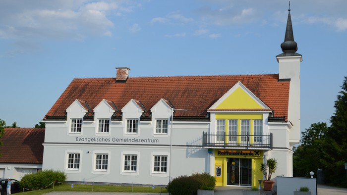Weißes Gebäude mit rotem Dach und Kirche daneben
