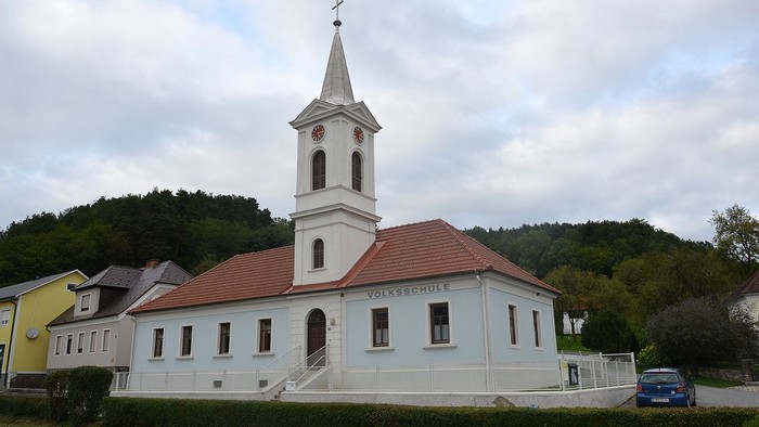 Kleine Kirche mit Uhrturm und rotem Dach in ländlicher Umgebung