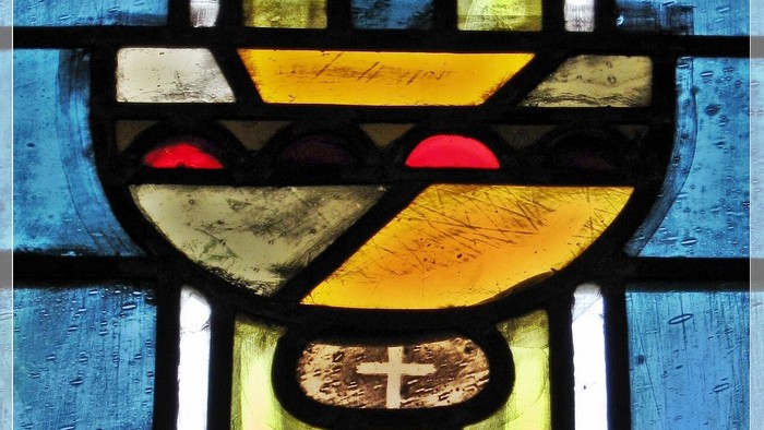 Buntglasfenster mit der Darstellung eines Kelchs mit Kreuz auf blauem Hintergrund.