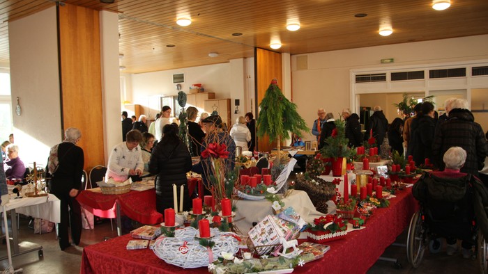 Ein Raum mit vielen Personen in einem Saal. In der Mitte steht ein großer, weihnachtlich geschmückter Tisch.