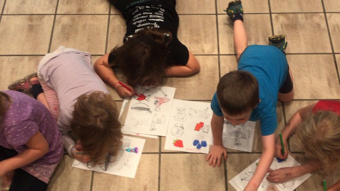 Kinder malen auf dem Boden mit Stühlen drumherum.