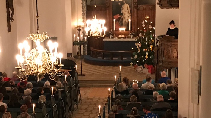 Kirkeinteriør med menighed, lysekroner og alter.