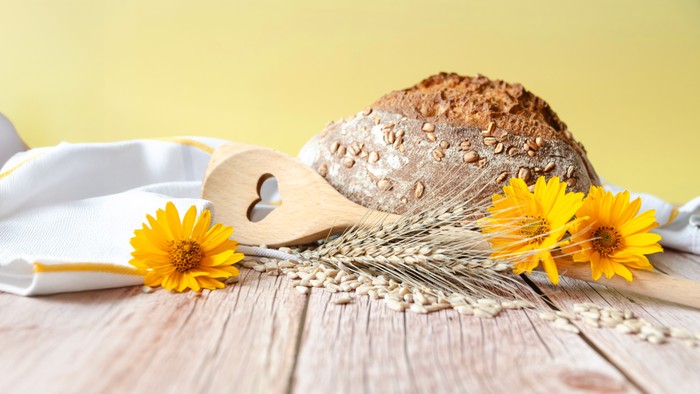 Ein Brot, ein Holzlöffel mit Herz und gelbe Blumen