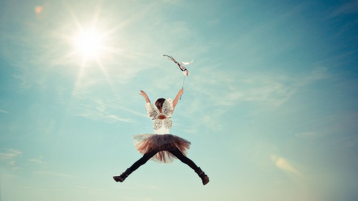 Ein Mädchen in einem rosa Kleid schwebt im Himmel mit einem Vogel.