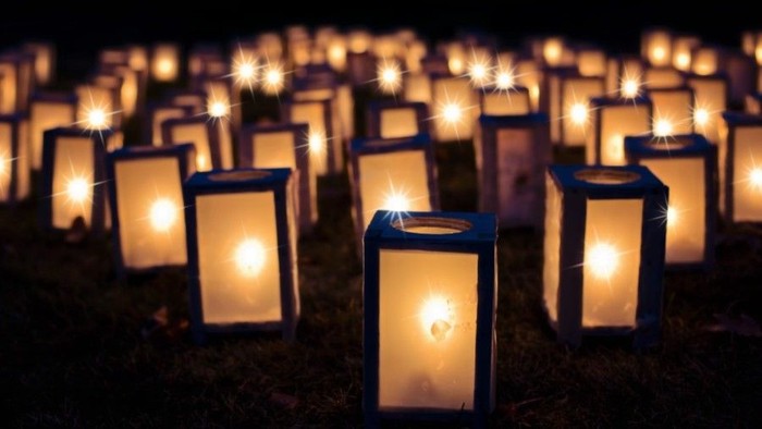 Talrige tændte lanterner placeret tæt sammen på græsbunden om natten.