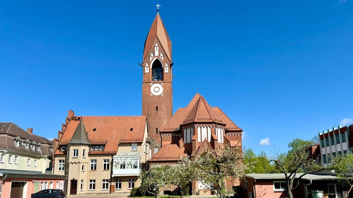 Bild zeigt eine Kirche mit hohem Turm und Uhr, umgeben von einem gepflegten Garten.
