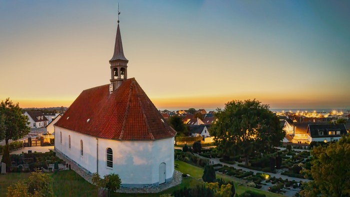 En hvid kirke med rød tag og tårn i en landsby ved sundet