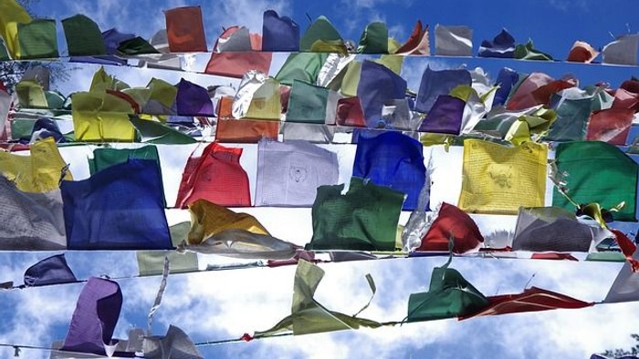 Bunte Gebetsfahnen im Wind vor blauem Himmel – Symbol für internationalen Gottesdienst.