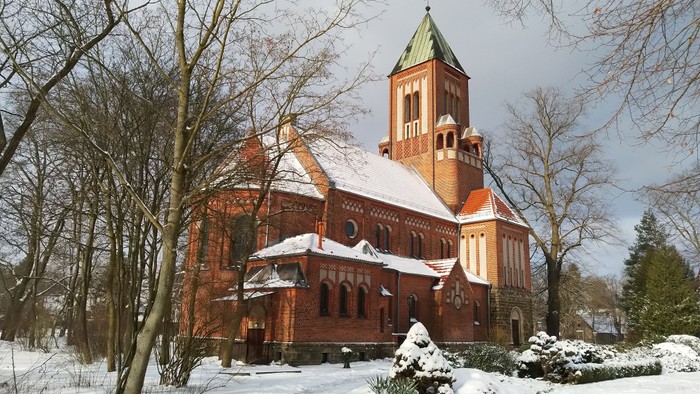 Ein rotes Backsteingebäude mit grünem Turm steht im Schnee, umgeben von kahlen Bäumen