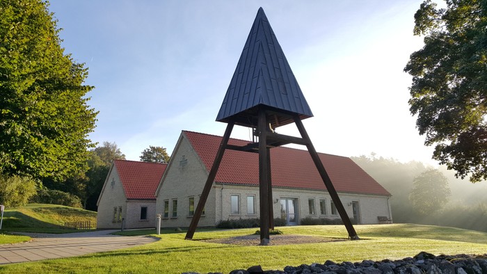 En moderne kirke med et karakteristisk tårn og røde tag i en træket skovlandskab