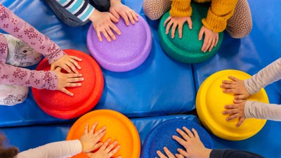 Kinder spielen im Kreis mit bunten Hockern auf einer blauen Matte