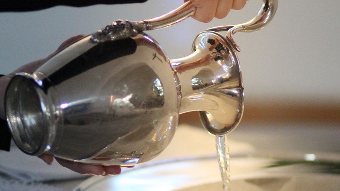 Vand fra sølvkande hældes i dåbsfad