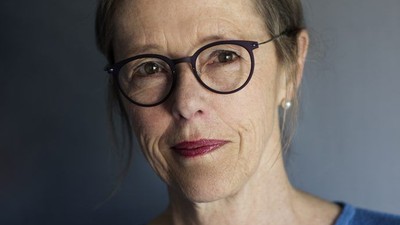 En kvinde med kort hår, briller og et neutralt udtryk iført en blå sweater.