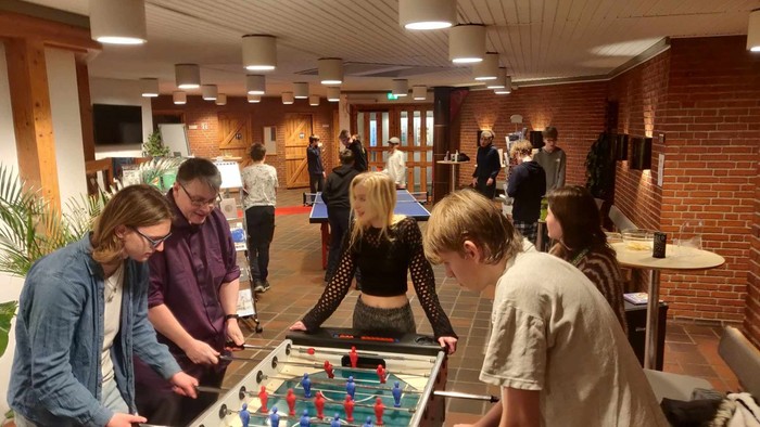 En gruppe unge spiller fodboldbillard i et lokal med mur af røde mursten.