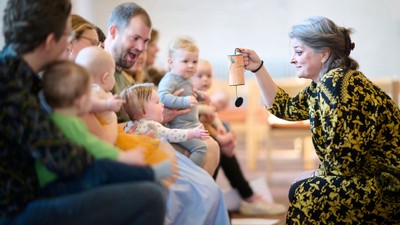 En kvinde i en mønstret kjole interagerer med børn under en livlig, uformel sammenkomst eller begivenhed.