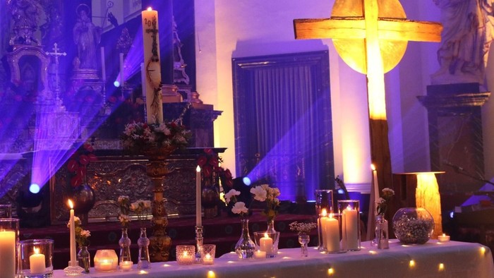 Eleganter Altar, geschmückt mit Kerzen, Blumen und religiösen Statuen unter farbiger Beleuchtung.
