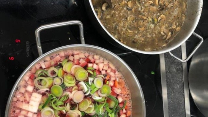 Zwei Töpfe köcheln auf dem Herd: einer mit Meeresfrüchtebrühe, der andere mit gewürfeltem Fleisch, Zwiebeln, Karotten und Kräutern.