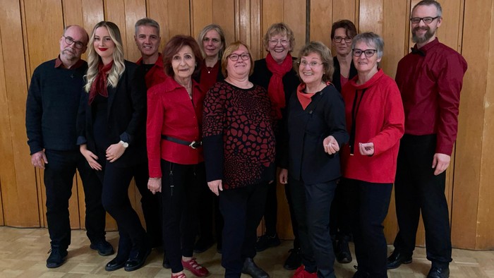 Gruppe von Personen, die gemeinsam posieren, in roter und schwarzer Kleidung, stehend vor Holztüren.