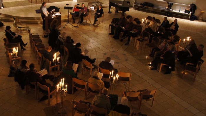 Eine Gruppe von Menschen sitzt in einem Kreis und hält Kerzen, während einige Musiker in der Mitte spielen.