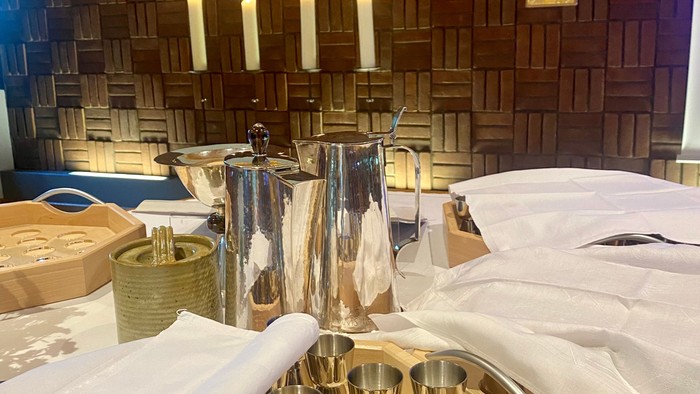 Ein Tisch mit silbernen Kelchen, Kerzenständern und einem goldenen Kreuz im Hintergrund