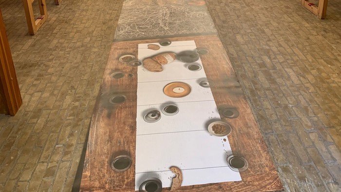 Moderne kirkeinteriør med træbænke, alterbord og kunstnerisk vægmaleri bag alteret.