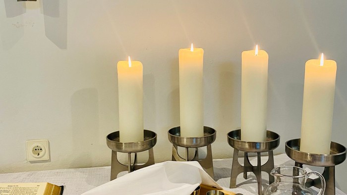 Weiße Kerzen in silbernen Haltern auf Tisch, daneben Wein und Buch