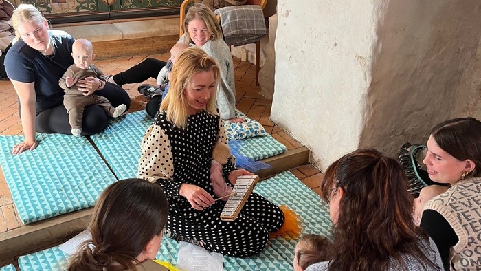 Forældre med deres babyer sidder på kirkegulvet og synger sange og remser