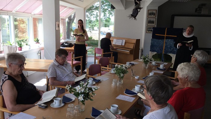 En gruppe af mennesker sidder ved et bord og ser på en kvinde, der står og synger.